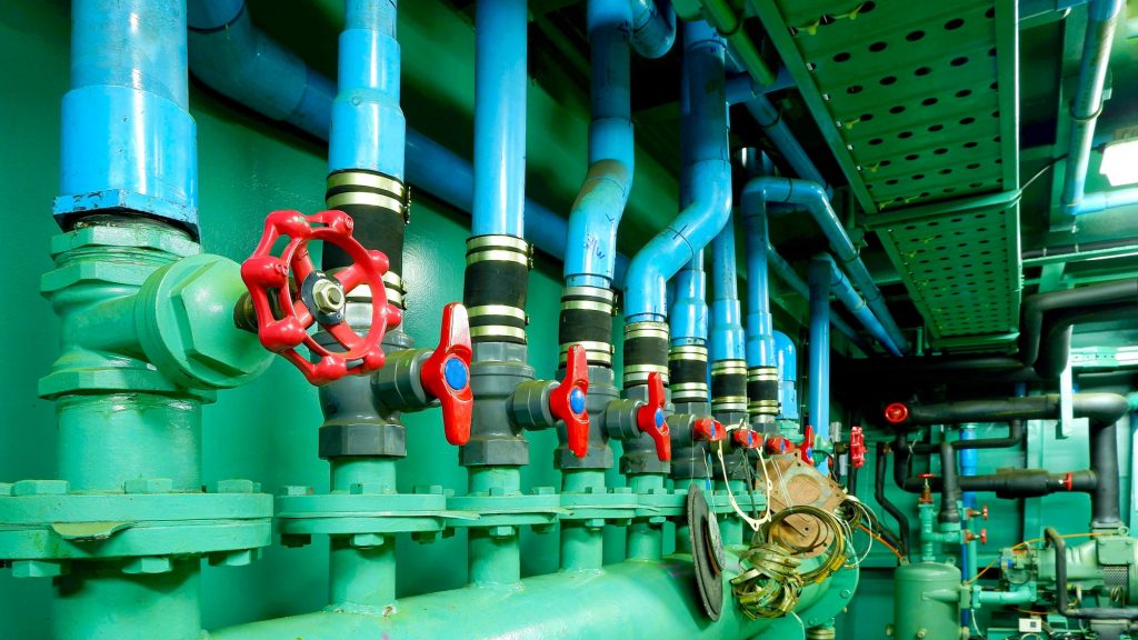 Focus at red gate valves with pipelines of main water pressure control in engine room of vessel